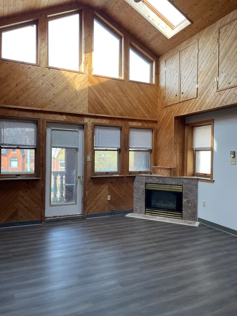 Unfurnished room with a vaulted wood ceiling, skylights and a fireplace.