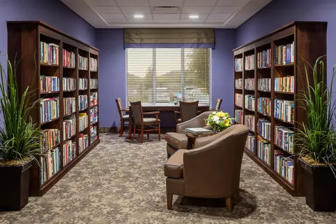 Library with bookshelves, armchairs and a table beside a window