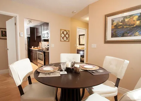 Round dining table with white chairs beside a kitchen and hallway