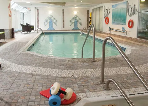 Indoor swimming pool with metal handrails and chairs beside tall windows