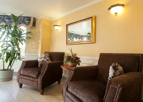 Two brown armchairs beside a plant and framed landscape painting