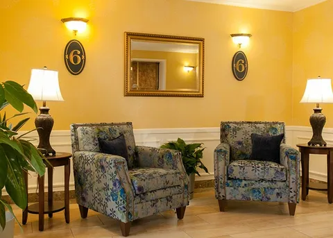Two patterned armchairs below a wall mirror between table lamps