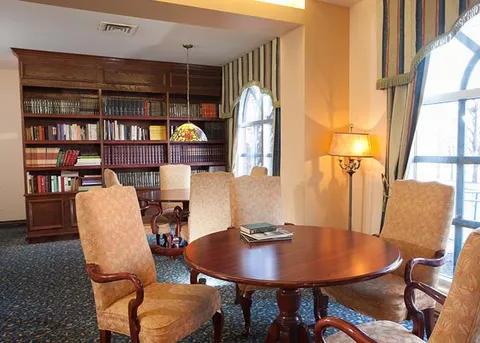 Library with bookshelves, upholstered chairs and a round wooden table