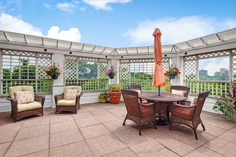 Patio with a pergola, wicker chairs, tables and flower planters.
