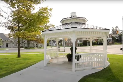 White gazebo with potted shrubs, lawn, a tree and a paved path