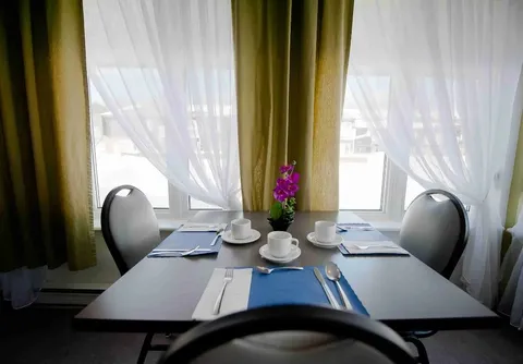 Dining table set with cups and cutlery beside a curtained window