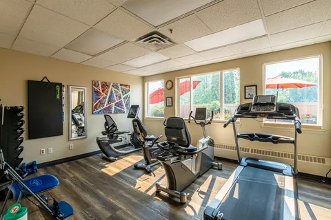 Fitness room with a treadmill, exercise bikes, dumbbells and windows