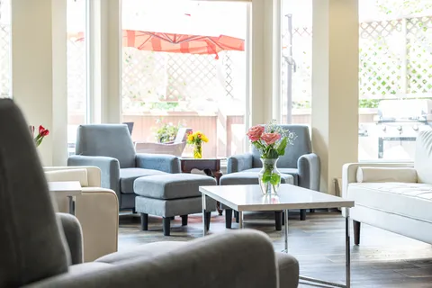 Armchairs and a white sofa beside large windows, with flowers on a coffee table