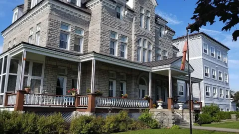 Stone building with a covered porch, white railings, steps and flowering planters