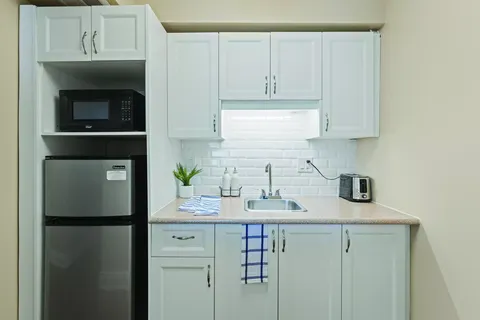Compact kitchenette with white cupboards, refrigerator and microwave