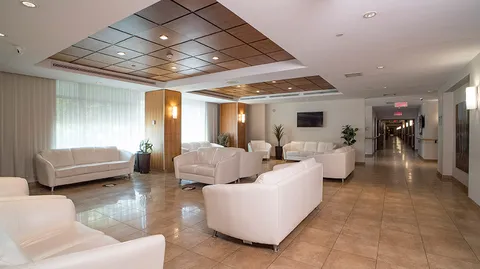 Common lounge with white sofas, tiled flooring and a wall-mounted television.