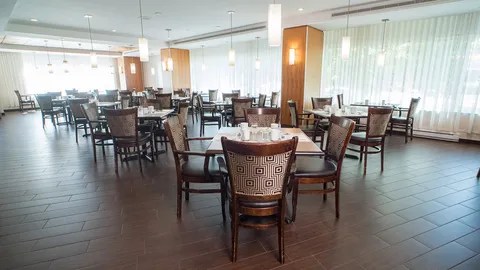 Dining room with wooden chairs, laid tables and full-height windows.