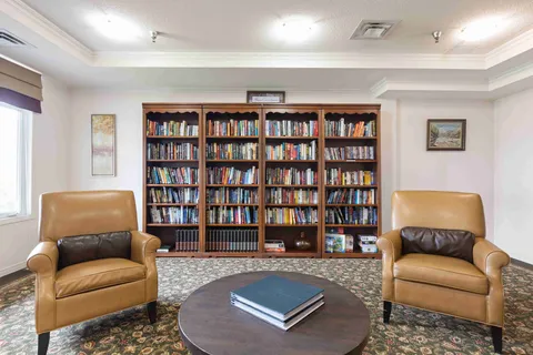Two leather armchairs and a round table in front of filled wooden bookshelves
