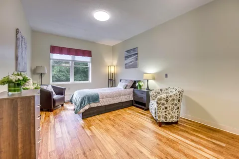 Bedroom with a bed, armchair, framed artwork and wooden floor