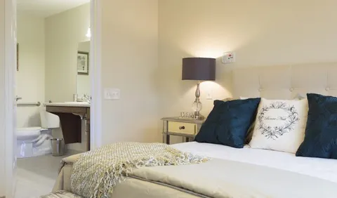 Bed with pillows beside a bedside lamp and open bathroom doorway