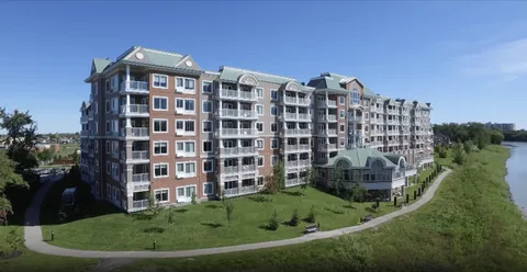 Multi-storey building with white balconies beside a river, lawn and curving path
