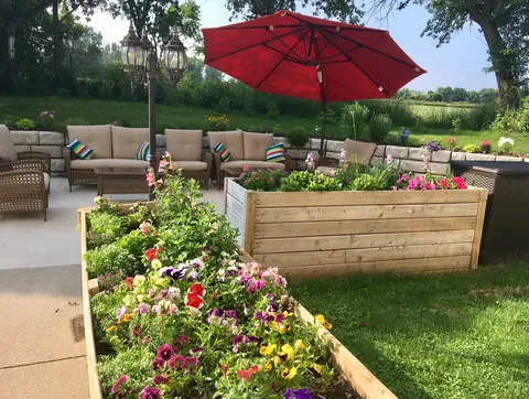 Raised flower beds beside a patio with chairs and an umbrella.
