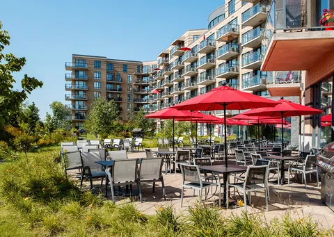 Building with glass balconies overlooking patio tables beneath red umbrellas