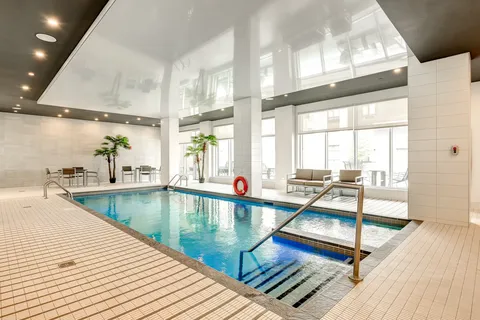 Indoor swimming pool with tiled surroundings, tall windows and deck seating