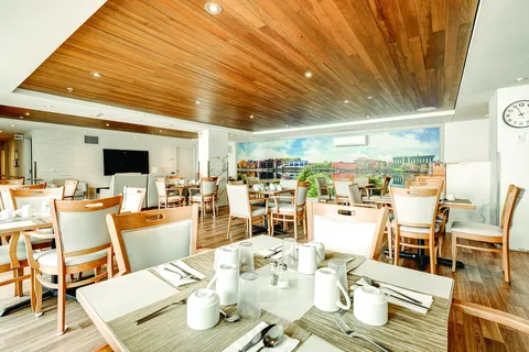 Dining room with set tables, pale chairs, wooden ceiling and a cityscape mural