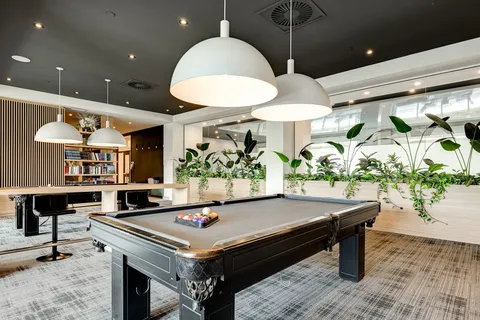 Pool table beside plants, bar stools and windows