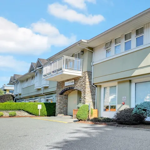 Two-storey residence with balconies, a stone entrance and shrubs beside the driveway