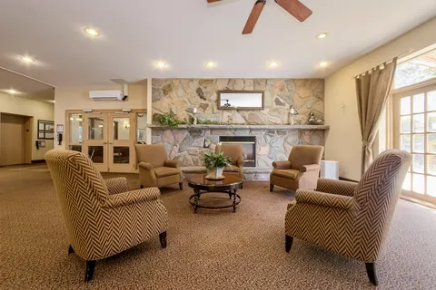 Lounge with upholstered chairs, a stone fireplace and glass doors.