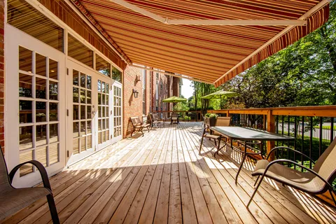 Covered wooden deck with tables and chairs beneath a striped awning.