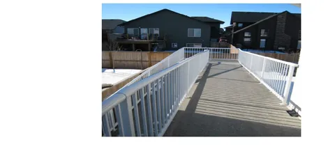 Access ramp with white railings leading through a fenced backyard