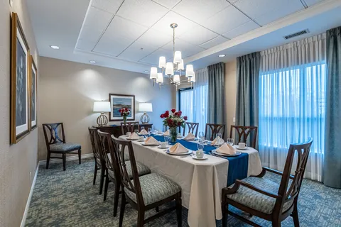 Dining room with a long set table, blue runner and curtained windows