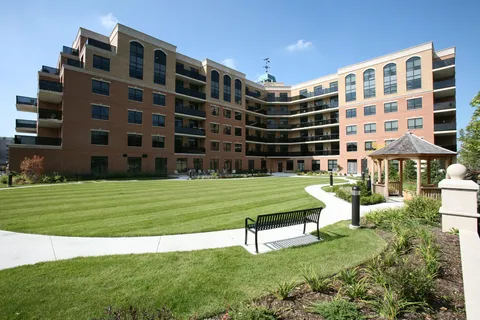 Brick residence surrounding a lawn with a gazebo, benches and a paved path