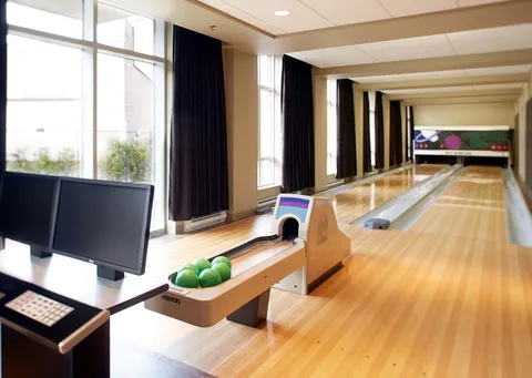 Bowling lane beside large windows with a scoring screen and green bowling balls