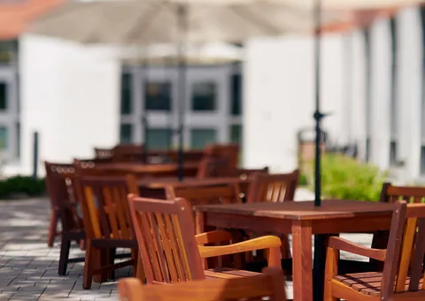 Wooden patio chairs and tables beside a planted bed and glass doors