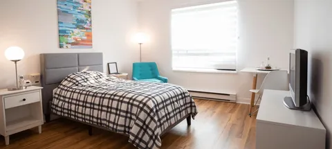 Bedroom with a checked bedspread, turquoise chair and television