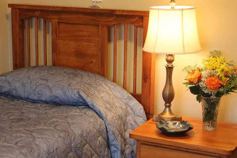 Bed with a wooden headboard beside a lamp and a vase of flowers