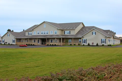 Beige residence with a covered porch, gabled roofs and a broad lawn