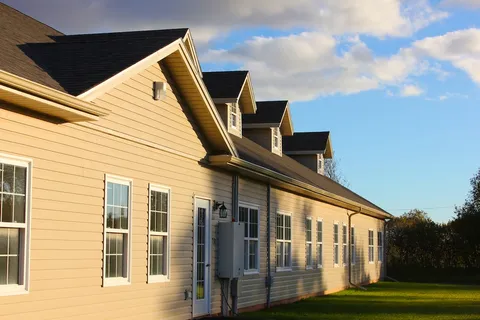 Side of a beige residence with white windows and a lawn