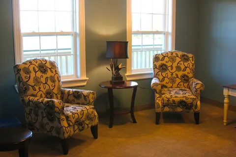Two floral armchairs beside windows and a round table with a lamp