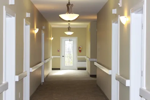 Carpeted hallway with handrails, wall lights and a glass panel door