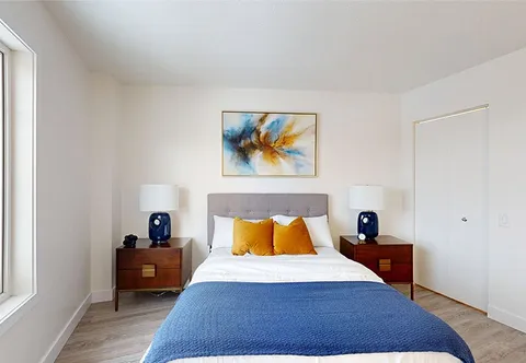 Bedroom with a blue bedspread, bedside tables and an abstract painting