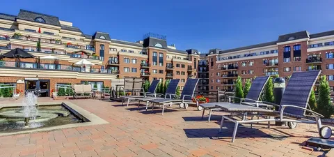 Residence buildings behind a paved terrace with reclining chairs and a fountain