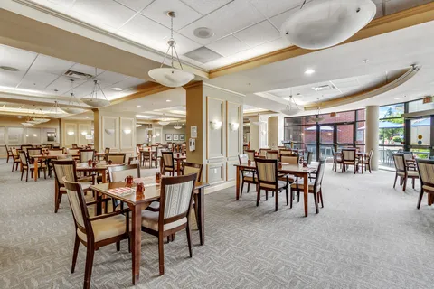 Dining room with tables, upholstered chairs and large windows.