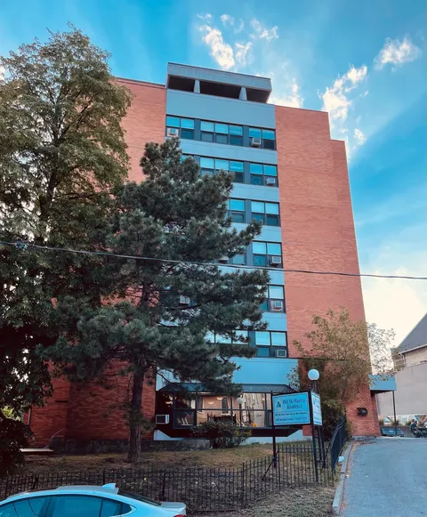 Multi-storey brick residence with front windows and trees beside the entrance.