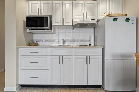 Kitchenette with white cabinets, a refrigerator, microwave and sink