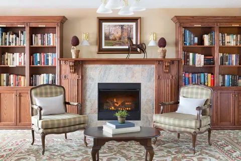 Library chairs and coffee table beside a fireplace and bookshelves.