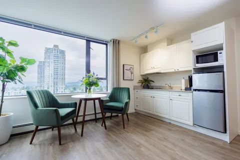 Kitchenette with white cabinets beside green armchairs and a round table