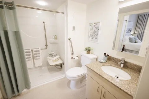 Bathroom with a shower, toilet, sink and a mirror reflecting a bedroom
