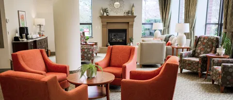 Common room with orange and patterned armchairs beside a fireplace
