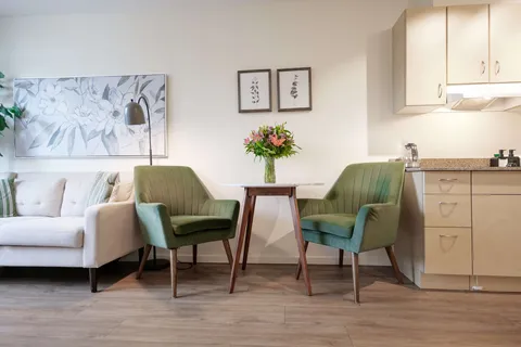 Sofa and two green chairs beside a small table and kitchenette