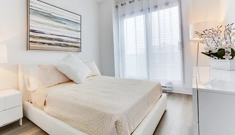 Bedroom with a white bed, a bedside lamp, curtains and abstract wall art
